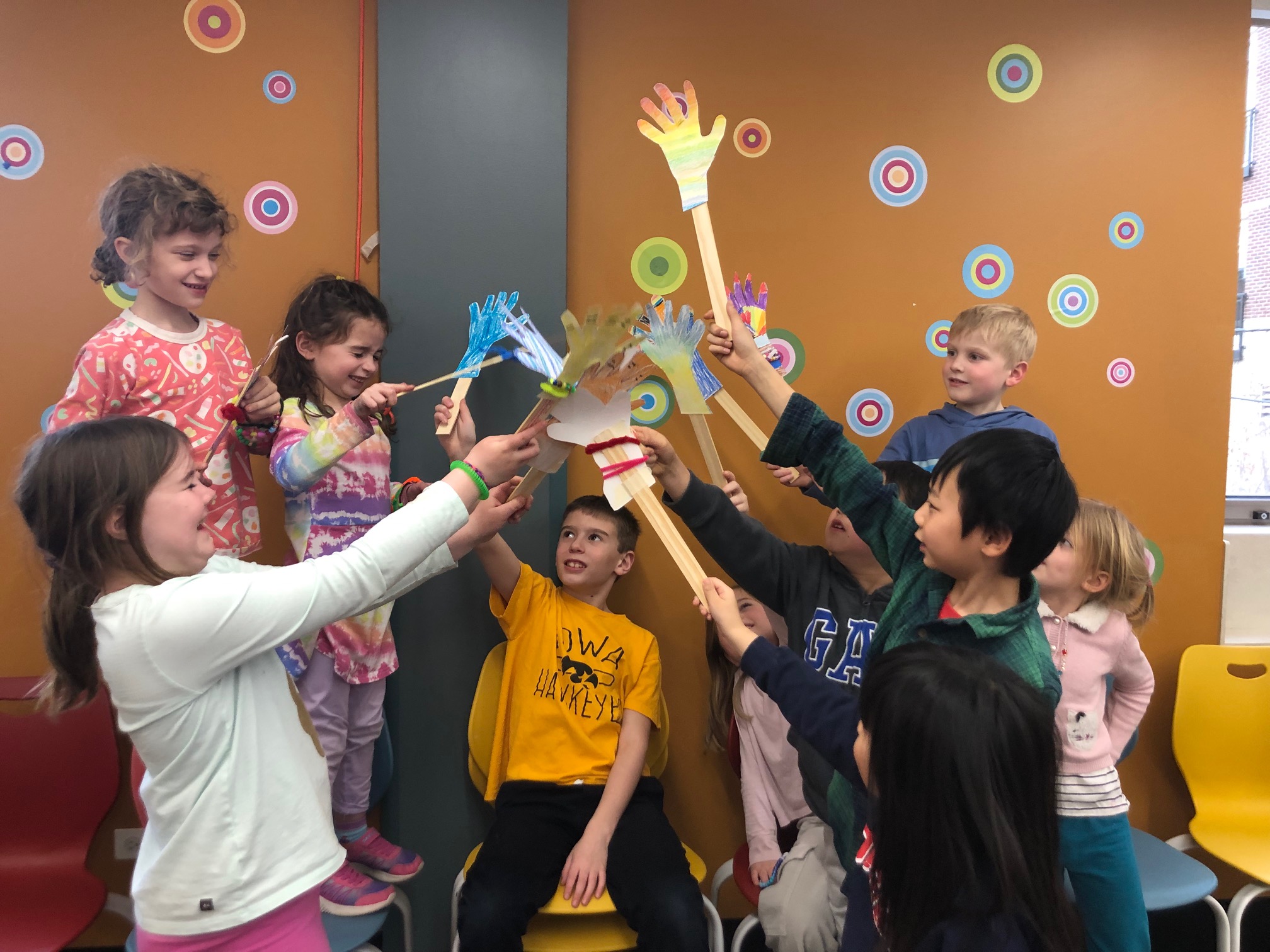 a group of smiling children holding up paper hands on sticks