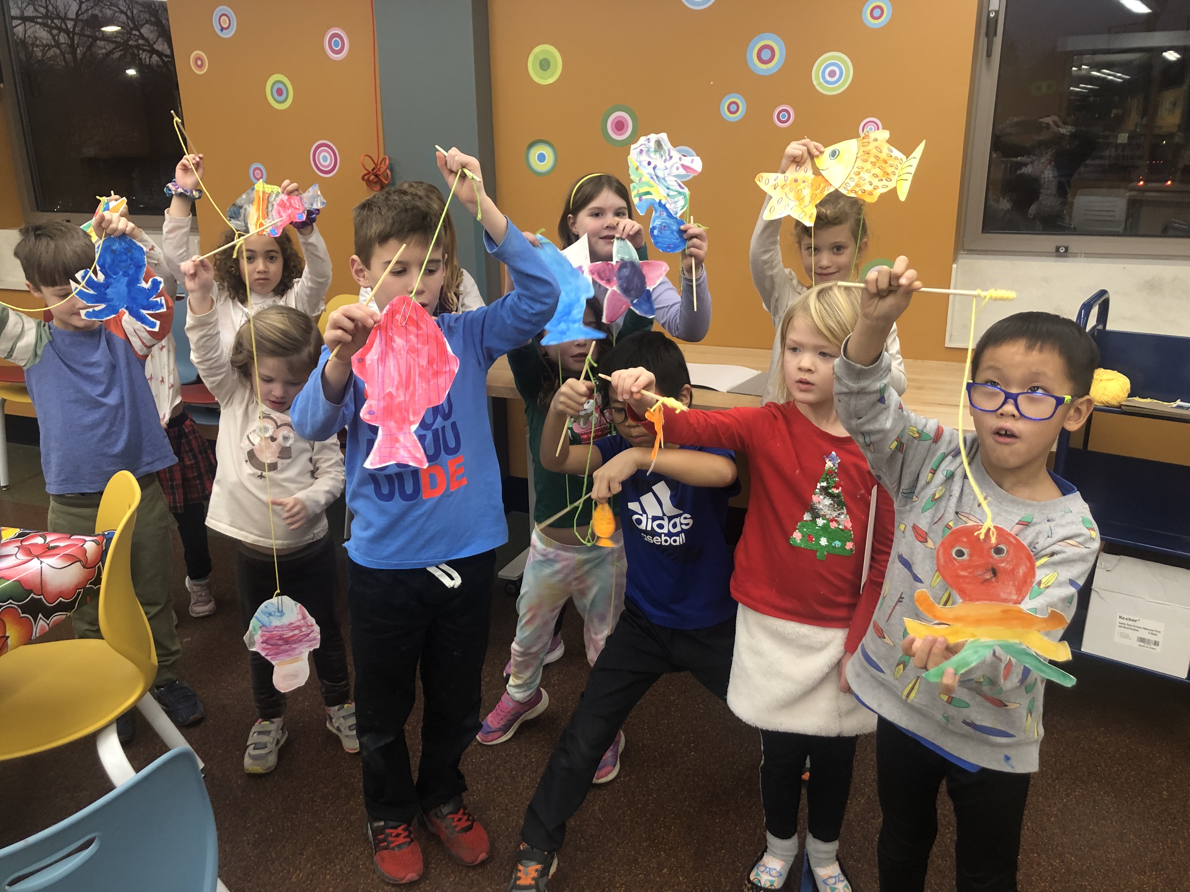 nine children holding colorful paper fishes on strings