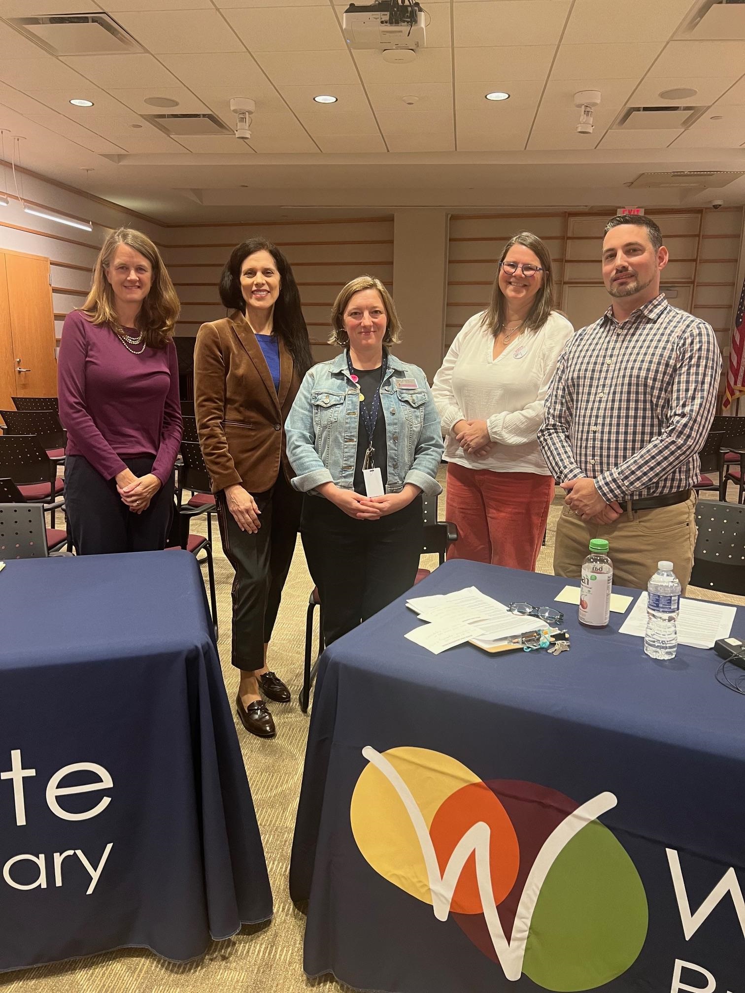 five white adults standing behind tables