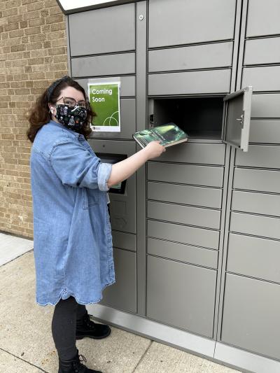 Image of a woman in a blue dress in front of a row of lockers placing a book in a locker.