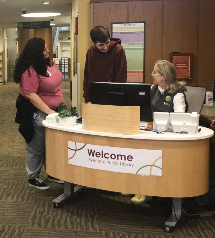 Two people talking to staff member at the Welcome desk of the library