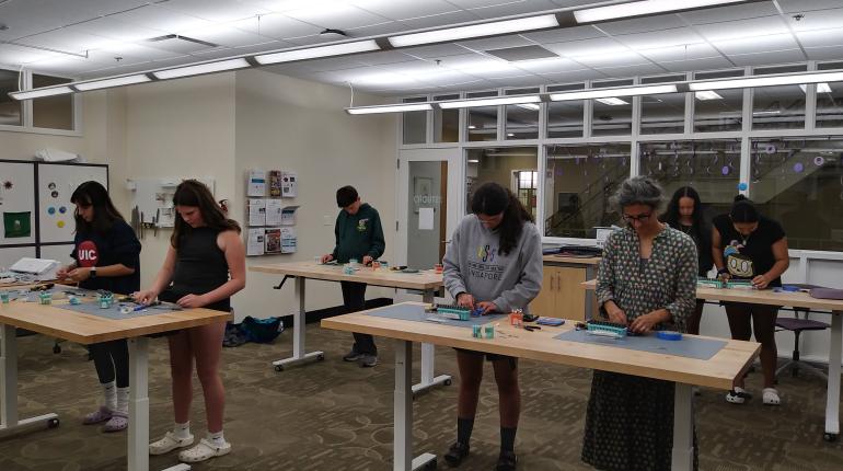 Patrons are standing at tables metal-stamping during a program in The Studio.